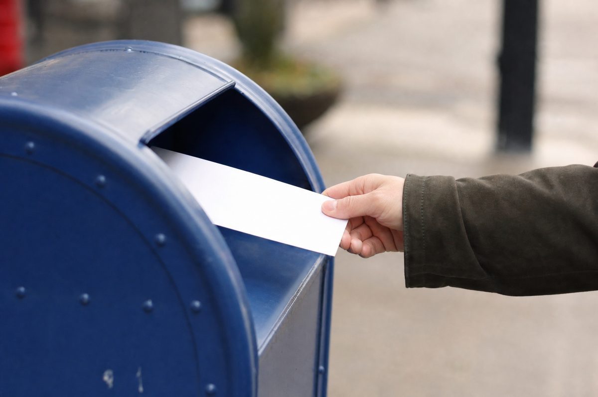A hand posting a plain envelope into a street mailbox